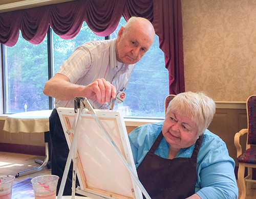 A volunteer assists a resident with her painting